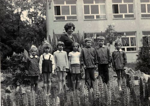 archiwalne zdjęcie 7 dzieci z nauczycielką na tle szkoły