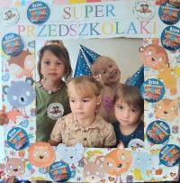 Dziewczynki z przedszkola pozują do zdjęcia w przygotowanej ramce z napisem dzień przedszkolaka