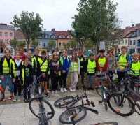 Uczniowie i  nauczyciel stoją w grupie w kamizelkach odblaskowych, przed nimi leżą rowery