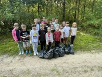 Uczniowie klasy pierwszej, drugiej i trzeciej stoją w grupce. Przed nimi leżą worki ze śmieciami