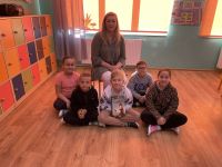 Uczniowie klasy trzej siedzą na podłodze, za nimi siedzi na krześle siedzi mama Karola