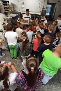 Dzieci stoją w grupie, pan piekarz częstuje dzieci pączkami