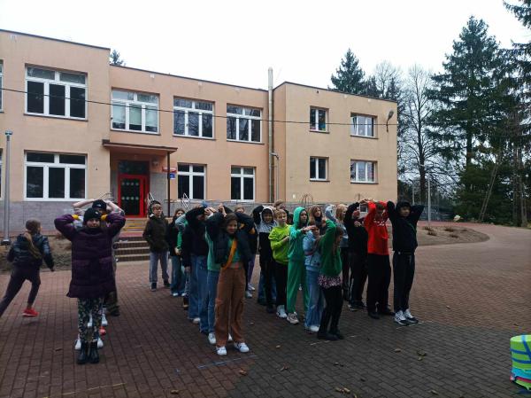 Uczniowie stoją w kilku rzędach za sobą na dworze przed budynkiem szkoły